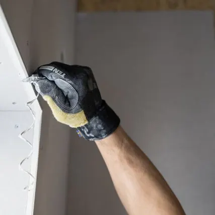 Mão enluvada tratando a junta de uma placa de drywall